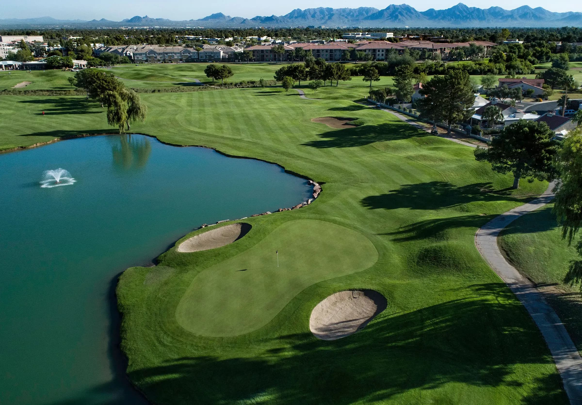 Aerial view of the first green at Stonecreek, beside a lake with a fountain, with the mountains beyond