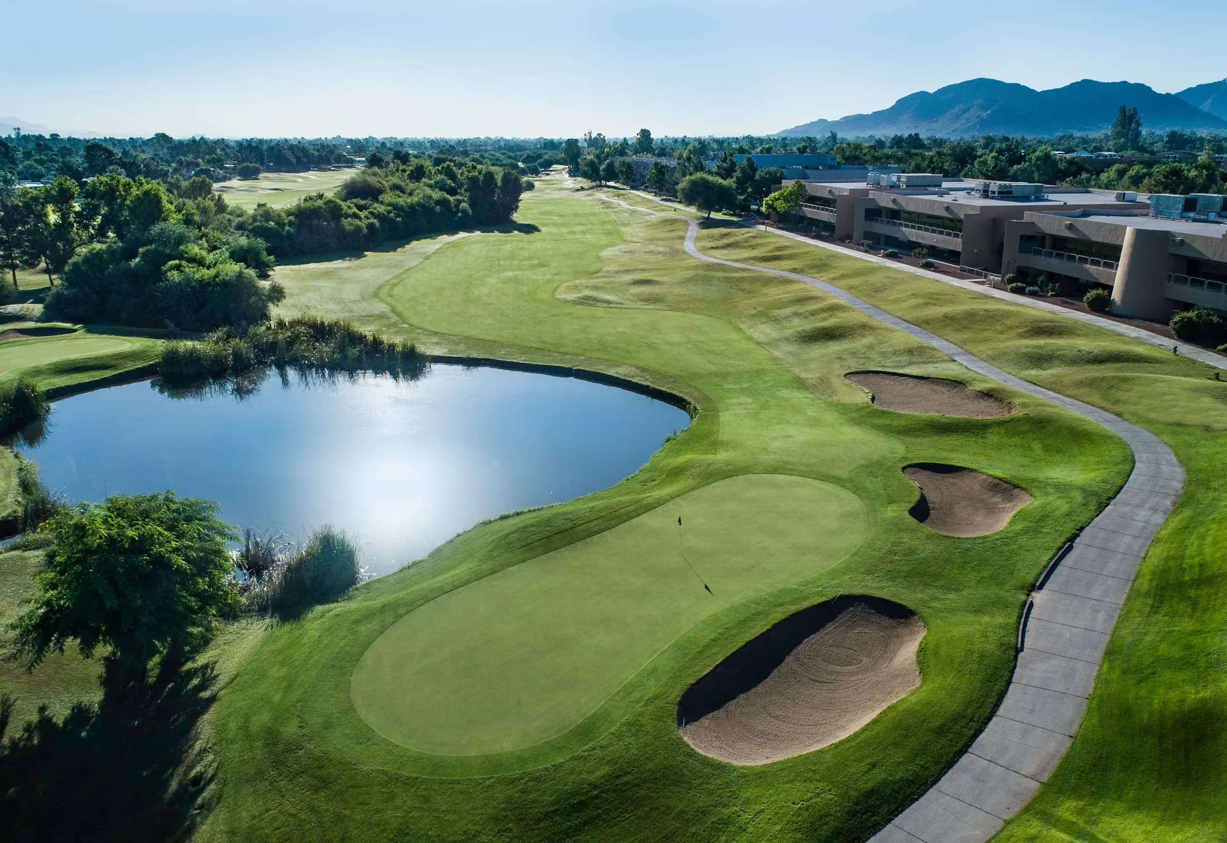 Aerial view of the sixteenth green beside a pond, guarded by bunkers